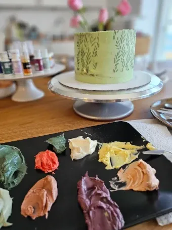 Green buttercream cake in progress with colour palette and decorating tools on a worktable